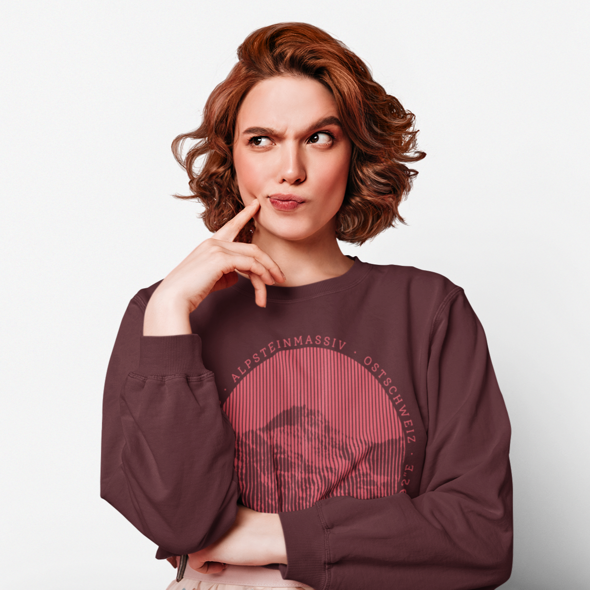 Rothaarige, junge Frau in einer nachdenklichen Pose. Sie trägt ein kastanienbraunes Sweatshirt mit dem Aufdruck des Säntis-Gipfels.