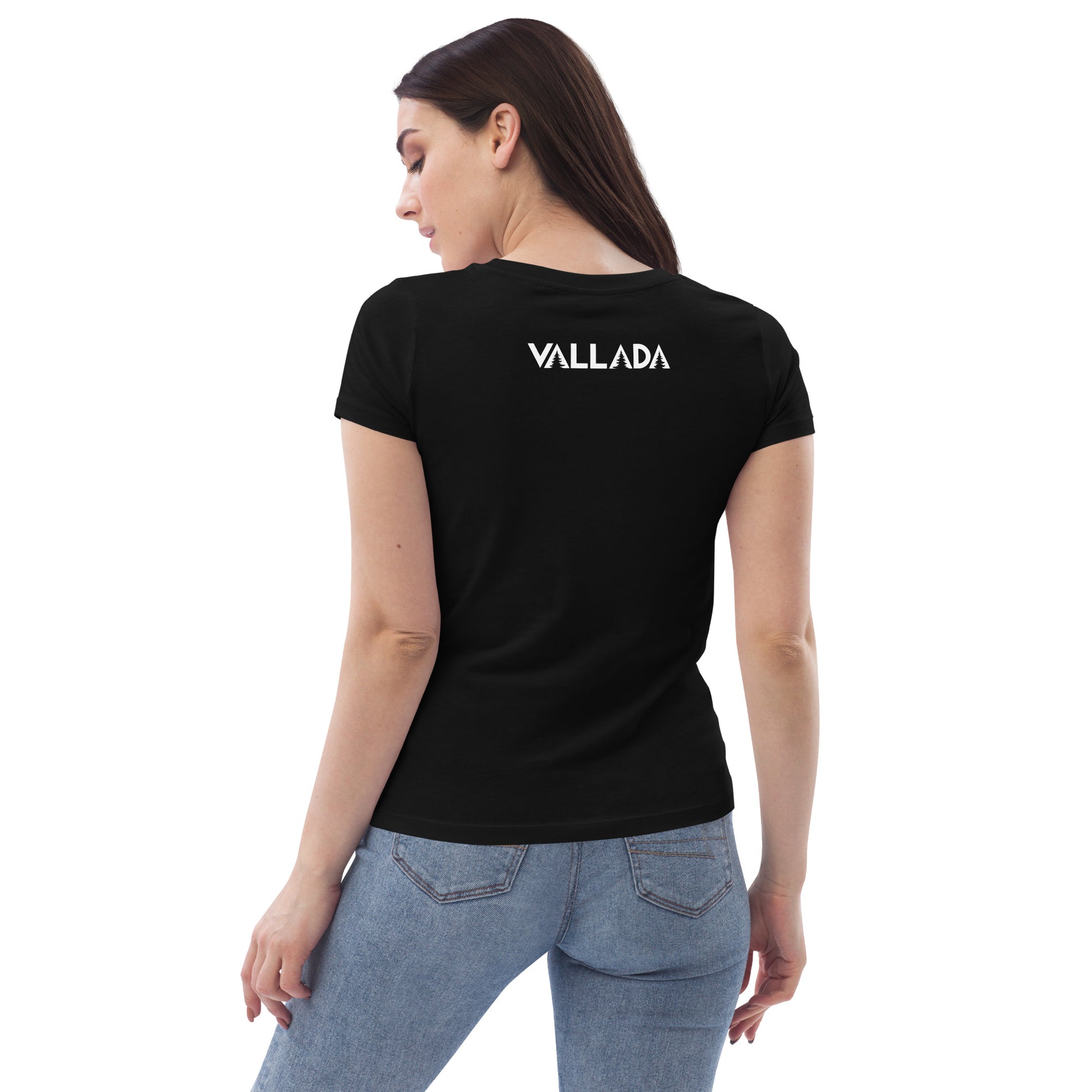 Sie steht mit dem Rücken zu uns, so dass wir die Rückseite des schwarzen T-Shirts mit dem Vallada-Logo sehen können. Zum T-Shirt tägt sie eine blaue, enge Jeans.