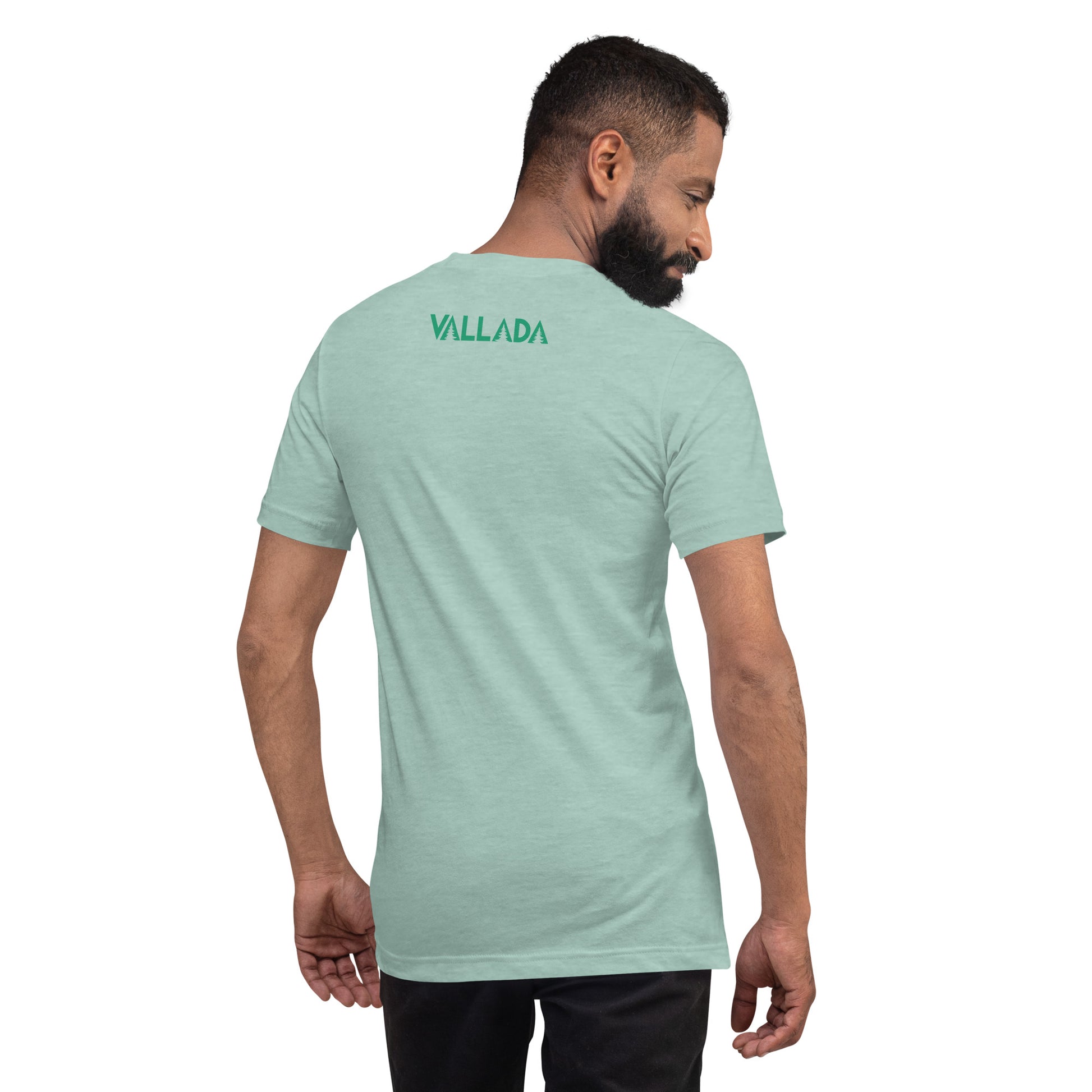 Wir sehen einen bärtigen Mann in Jeans und T-Shirt von hinten. Auf dem oberen Rückenteil seines T-Shirts sehen wir den Schriftzug der Marke "VALLADA".